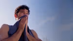 Close-up of a person outdoors holding a towel to their face under a clear blue sky.