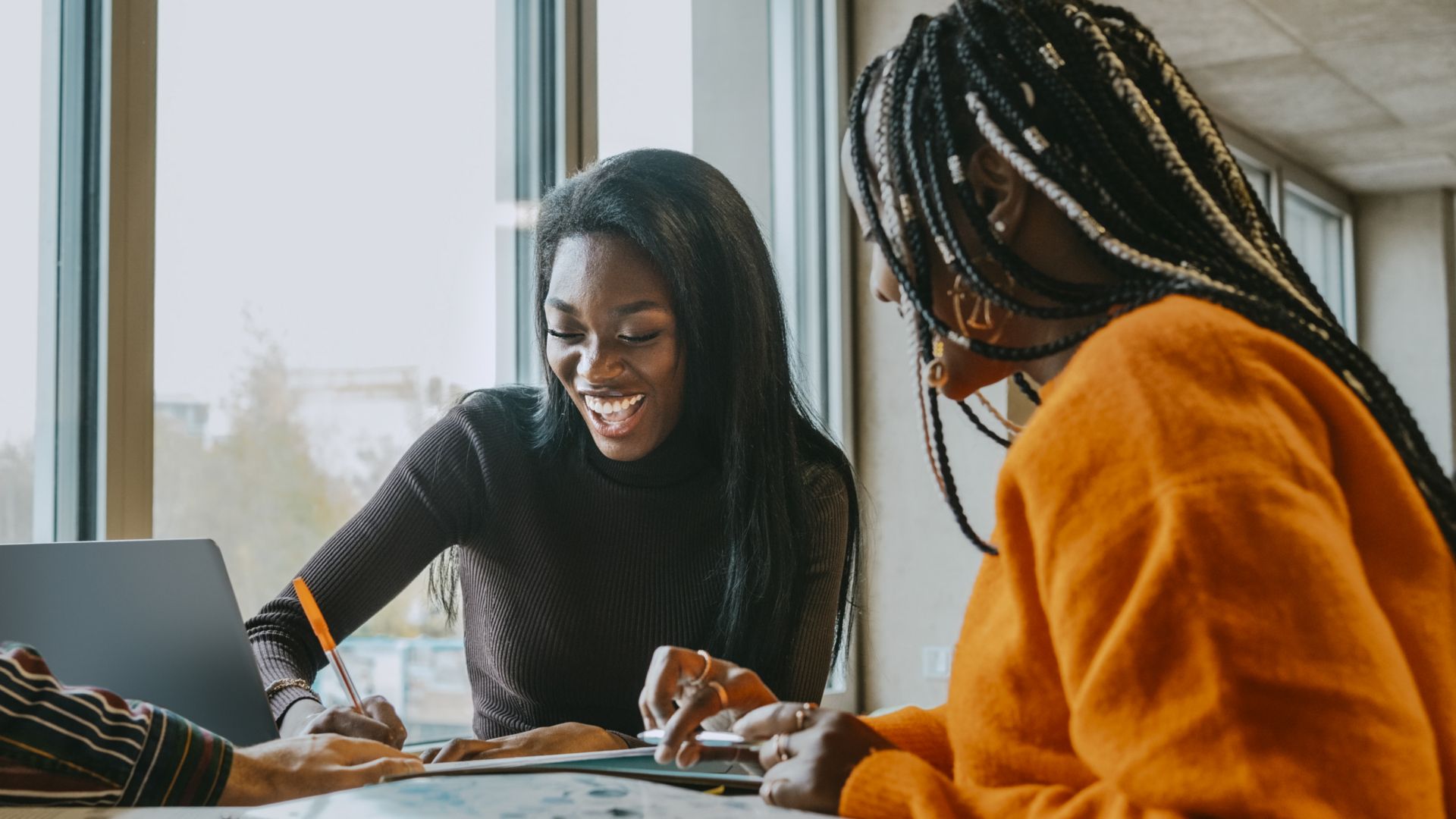 Two women working together at a desk, researching online and making notes