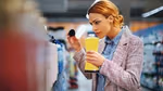 A lady in a shop smells the fragrance of a product having taken the lid off.