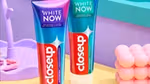 Two tubes of Closeup White Now toothpaste standing on a pastel bathroom counter with a pink toothbrush in the foreground.