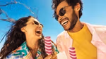 A woman and man, both with dark hair and sunglasses, are smiling at each other while each holds a Twister ice cream