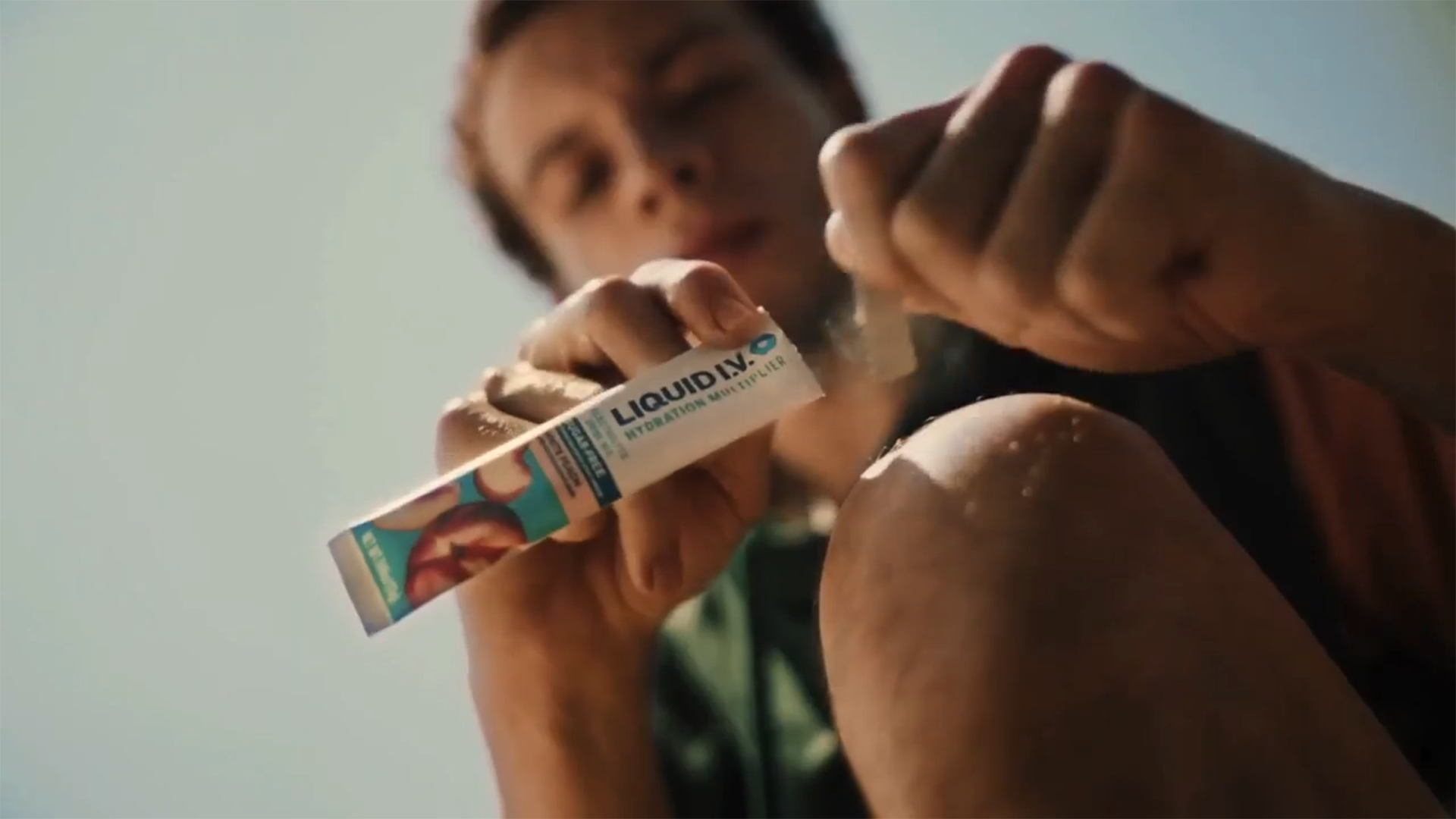 A man squatting and tearing open a sachet of Liquid I.V.