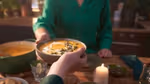 Cropped hand handing a bowl of pumpkin soup over a wooden table