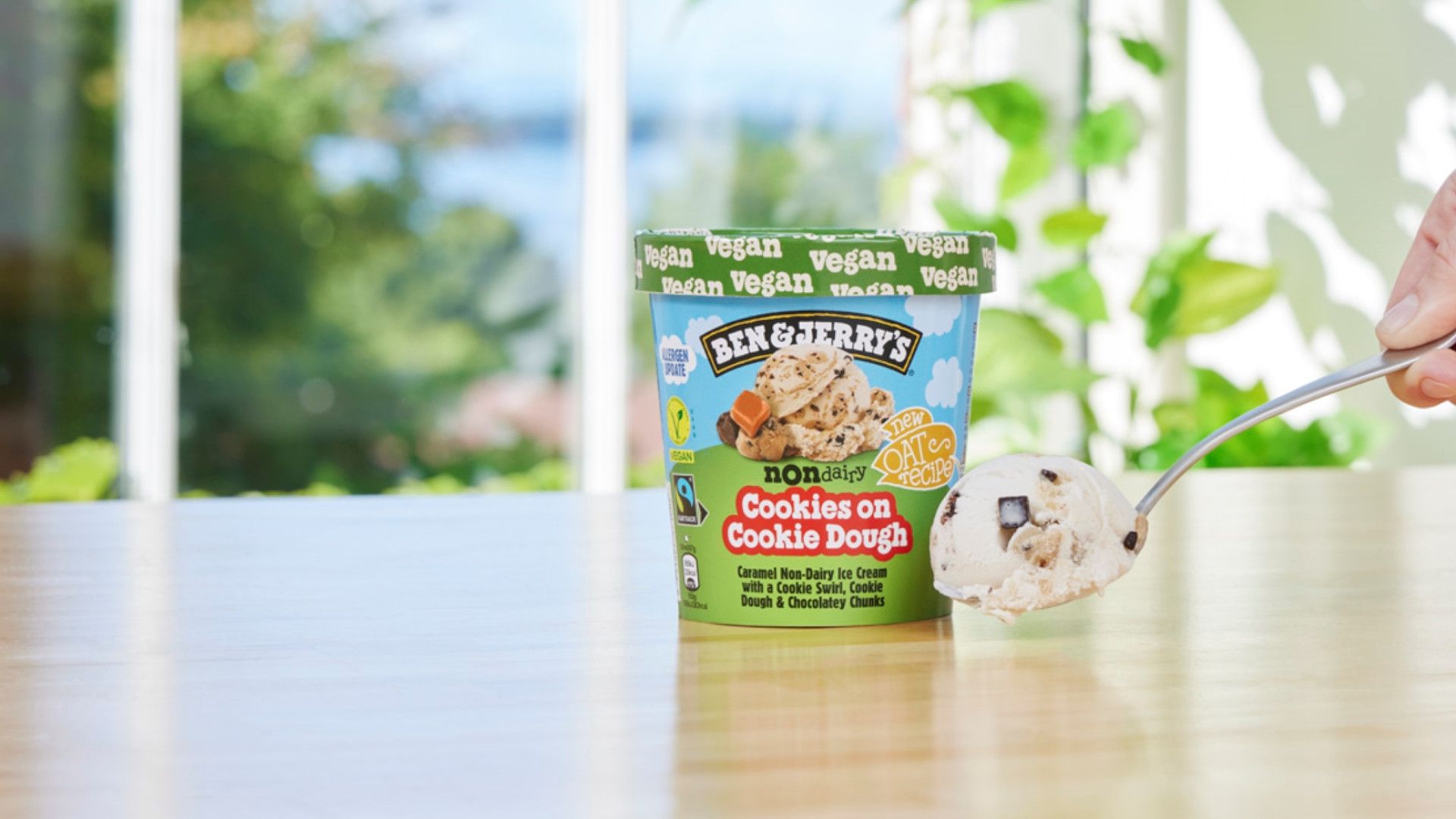 Ben & Jerry’s non-dairy Cookies on Cookie Dough tub with new oat base and a hand holding a smooth rich spoonful