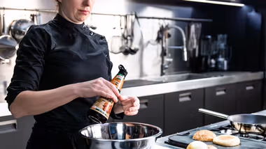 Female chef in professional kitchen pouring bottle of Knorr Intense Flavours into mixing bowl.