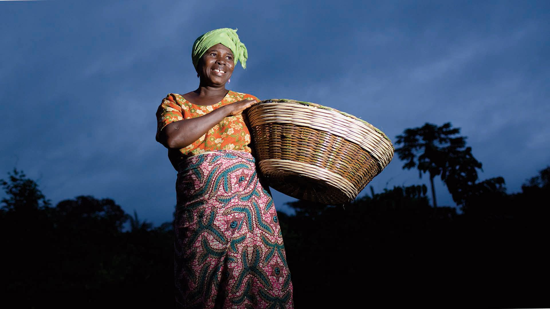 A smiling woman carrying a basket against an African sunset 