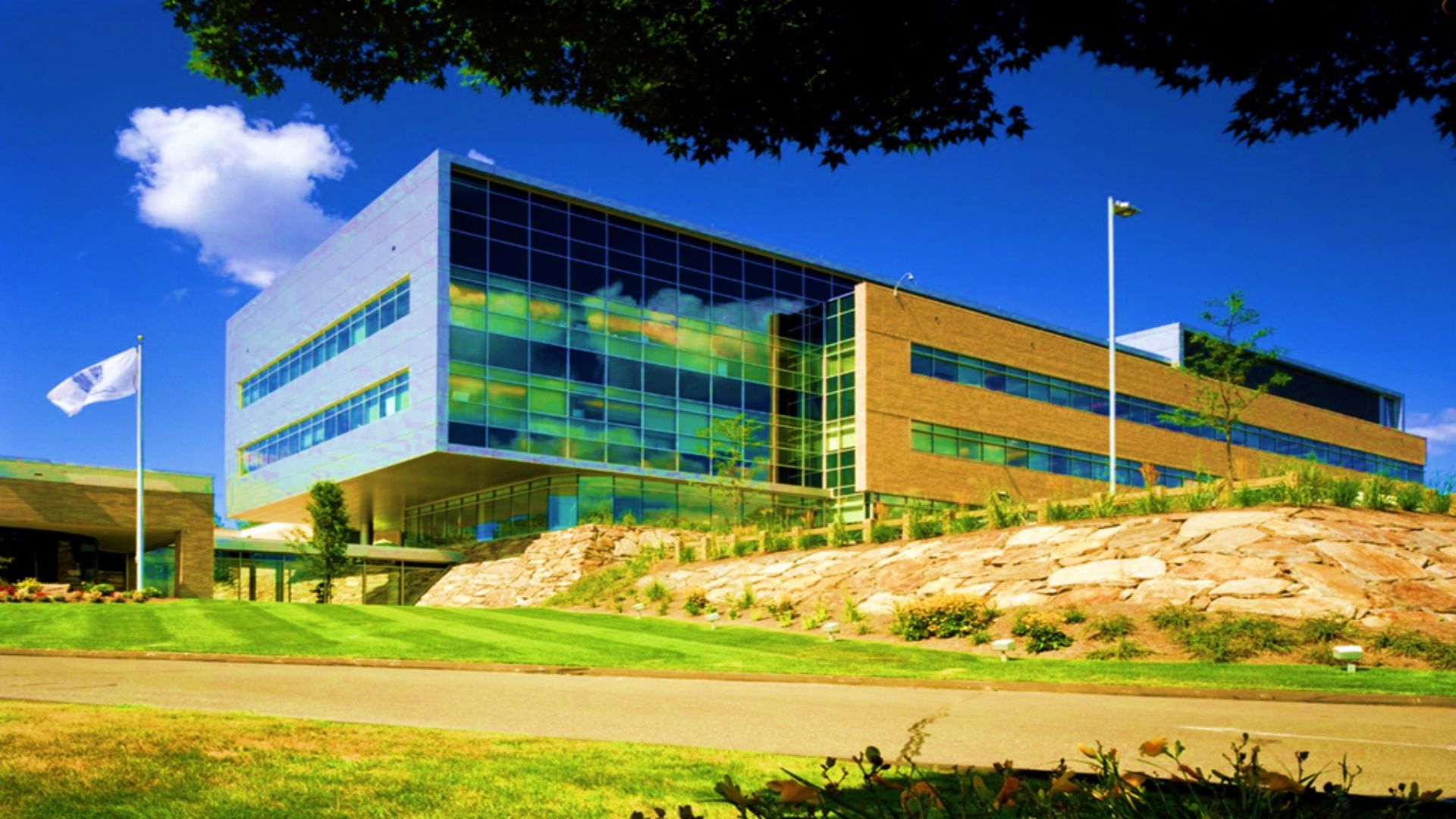 The exterior of an office building built on a hill. One section is mainly glass with a grey wall, while the rest is red brick. There is a flag on a pole displaying the Unilever logo.