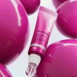 A pink tube of Vaseline Gluta‑Hya Lip Serum with a glossy applicator, surrounded by large, shiny pink spherical shapes on a soft light background.