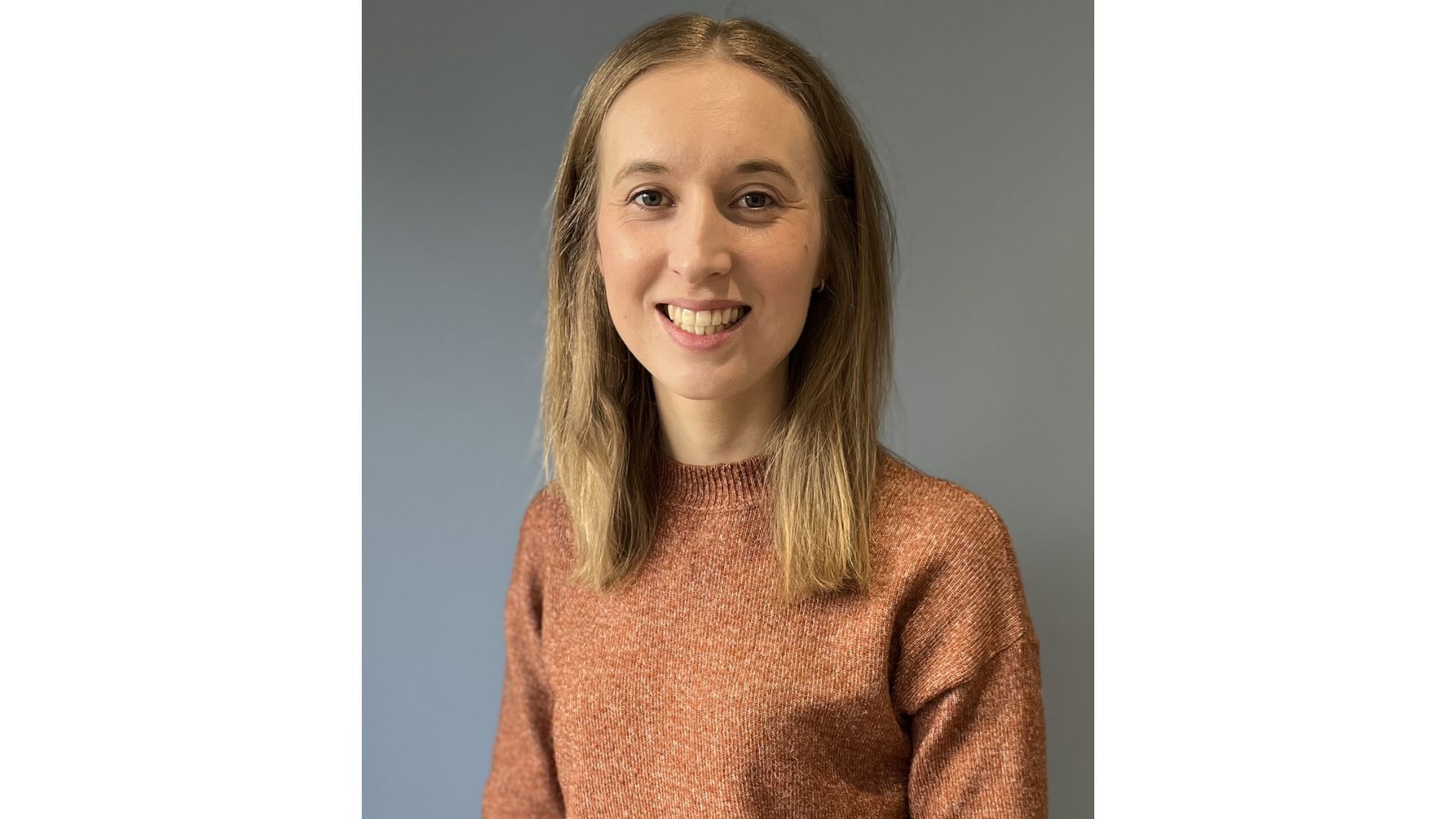 Portrait of Simone Pyle, who is a blonde-haired woman wearing an orange jumper