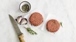 Two of The Vegetarian Butcher’s raw burgers on a plate with pepper and garnish being prepped for cooking