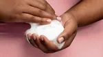 A closely cropped photo of a person in a pink top holding a Dove soap bar, with frothy white bubbles on their hands.