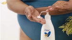 A woman in teal underwear pumps Dove Body Love lotion into her hand. Her face isn’t pictured. White bottle, Dove logo.