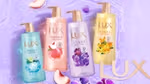 Four bottles of Lux Sparkling shower gel. One pink, one gold, one turquoise and one lilac, on a purple background with peach slices.