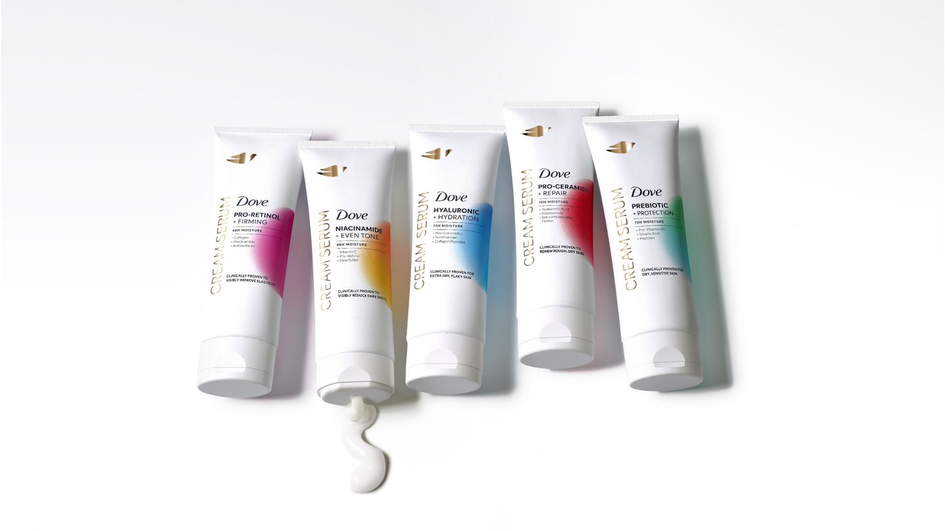 Dove cream serum products lined up on a white background. Some of the product squeezes out of one bottle.
