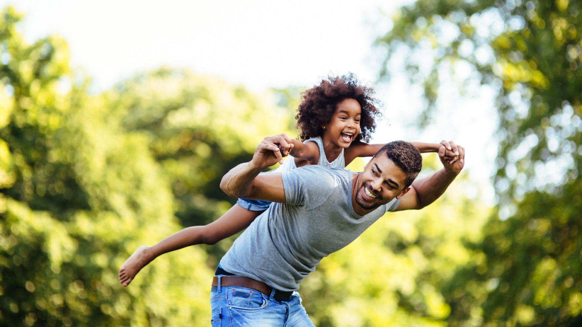 A man holding his child hands while on his back and laughing together
