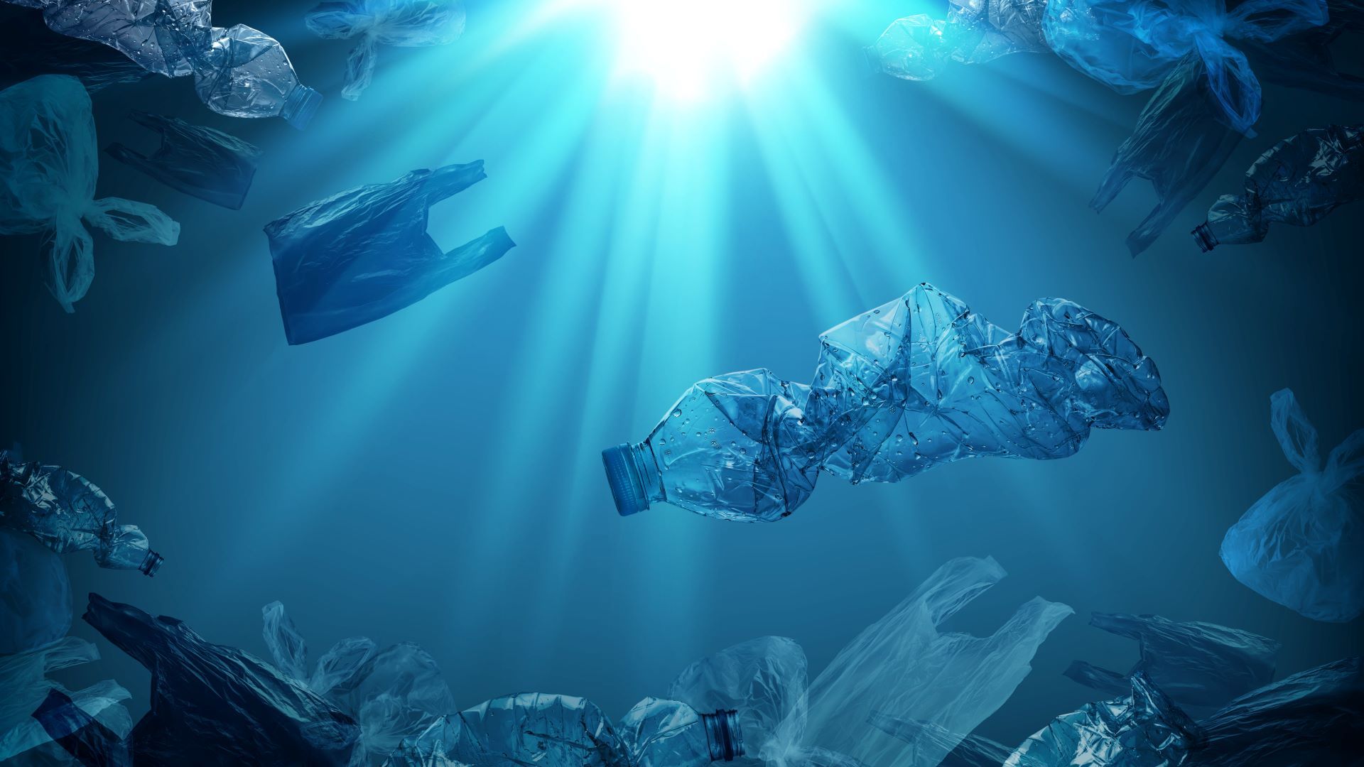 A photo of plastic bottles and bags floating in a blue ocean as sun beams into the water from above.