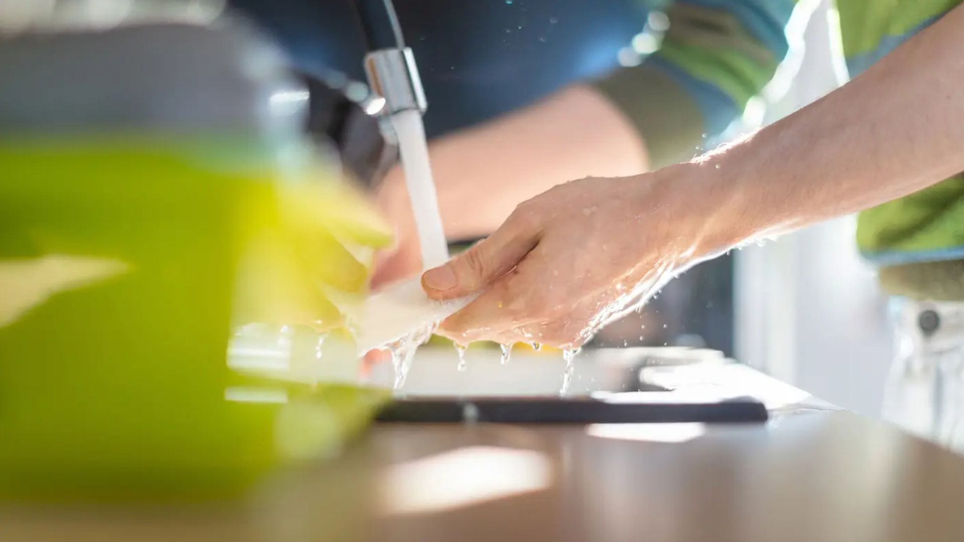 Close-up of a person’s hands washing a dish in the sink under running water.