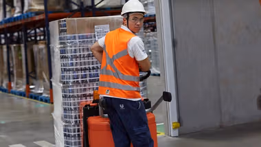 Worker in overalls and hard hat pulling a trolley across a factory floor