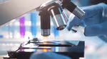 A close-up of a microscope. Someone wearing surgical gloves is holding a slide.