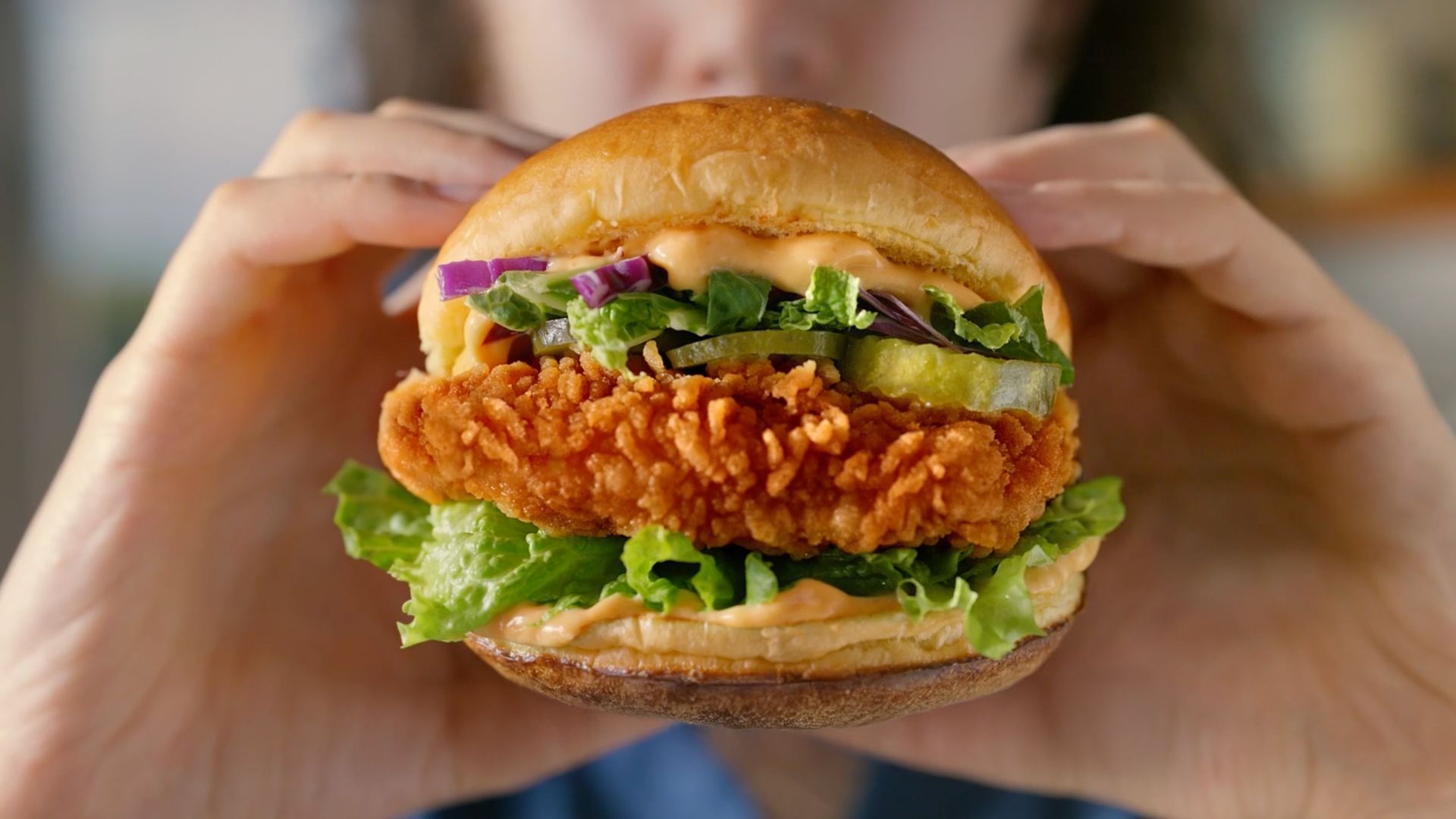 Person holding a crispy chicken sandwich with lettuce and pickles.
