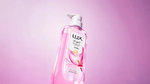 Close-up of a pink LUX Bright pump bottle with magnolia flower design, angled against a soft pink and lilac gradient background.
