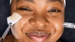 Young woman with melanin-rich skin undergoing a beauty treatment from a Dermalogica skincare professional