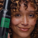 Woman holding Tresemmé Flawless Curls Mousse bottle with a smile.