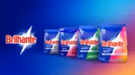 Four Brilhante laundry detergent packages displayed against a blue background. From left to right: green pack labelled ‘Higiene Total’, pink pack labelled ‘Limpeza Total’, purple pack labelled ‘Cuidado Total’, and white pack labelled ‘Delicadeza Total’. Each pack features bold red Brilhante branding and colourful accents.