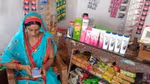 Indian woman store owner using mobile phone app while sitting next to shelves of consumer products.