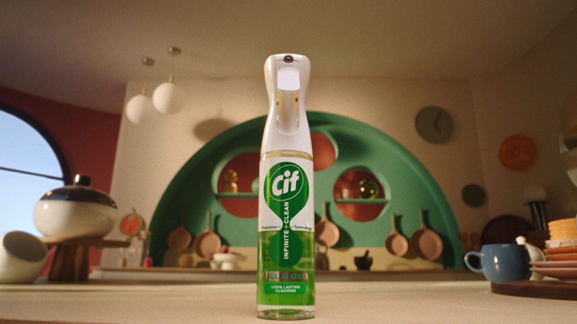 A bottle of Cif Infinite Clean spray sits on a kitchen countertop, with colorful cookware and decor in the background.