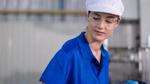 Person in glasses wearing white hard hat and blue overalls.