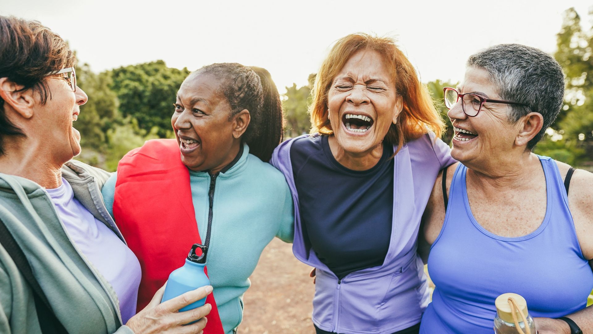 Four women laughing together outdoors.