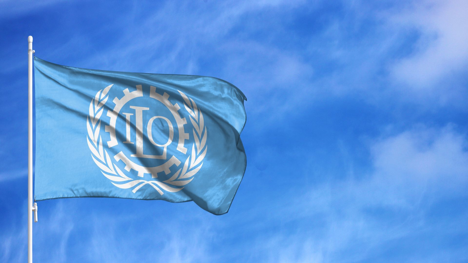 A light blue flag featuring the white logo of the International Labour Organization (ILO) against a bright blue sky.