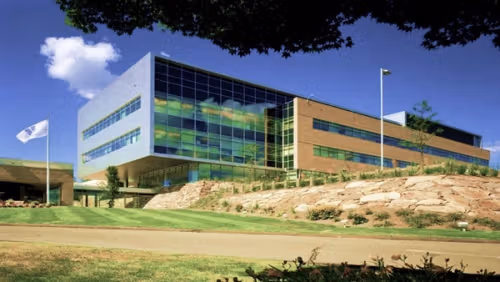 The exterior of an office building built on a hill. One section is mainly glass with a grey wall, while the rest is red brick. There is a flag on a pole displaying the Unilever logo.