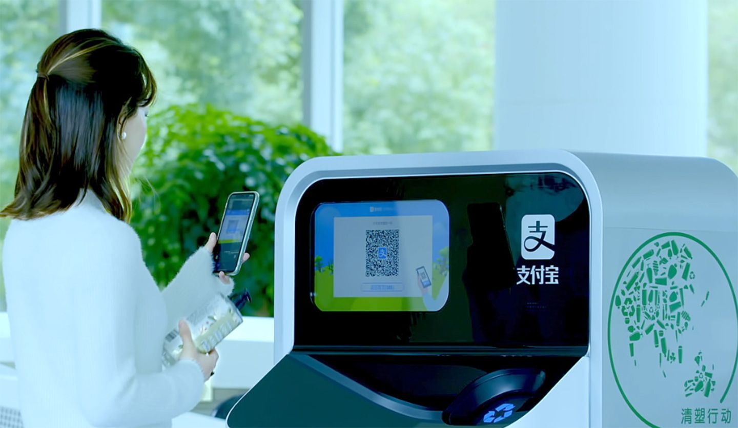 Woman holding plastic bottle ready to scan its QR code into an AI-enabled recycling and sorting machine