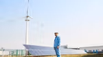 Worker in front of solar panels and wind turbine