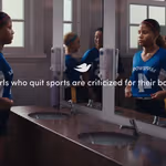A group of girls in sports uniforms stand in a locker-room–style bathroom with sinks and mirrors. One girl adjusts her uniform while others stand nearby, reflected in the mirrors. Text on the image reads: “1 in 2 girls who quit sports are criticized for their body type,” accompanied by a small dove icon.