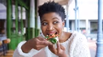 A woman eating a slice of pizza topped with vegetables and cheese