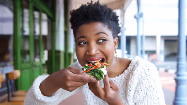 A woman eating a slice of pizza topped with vegetables and cheese