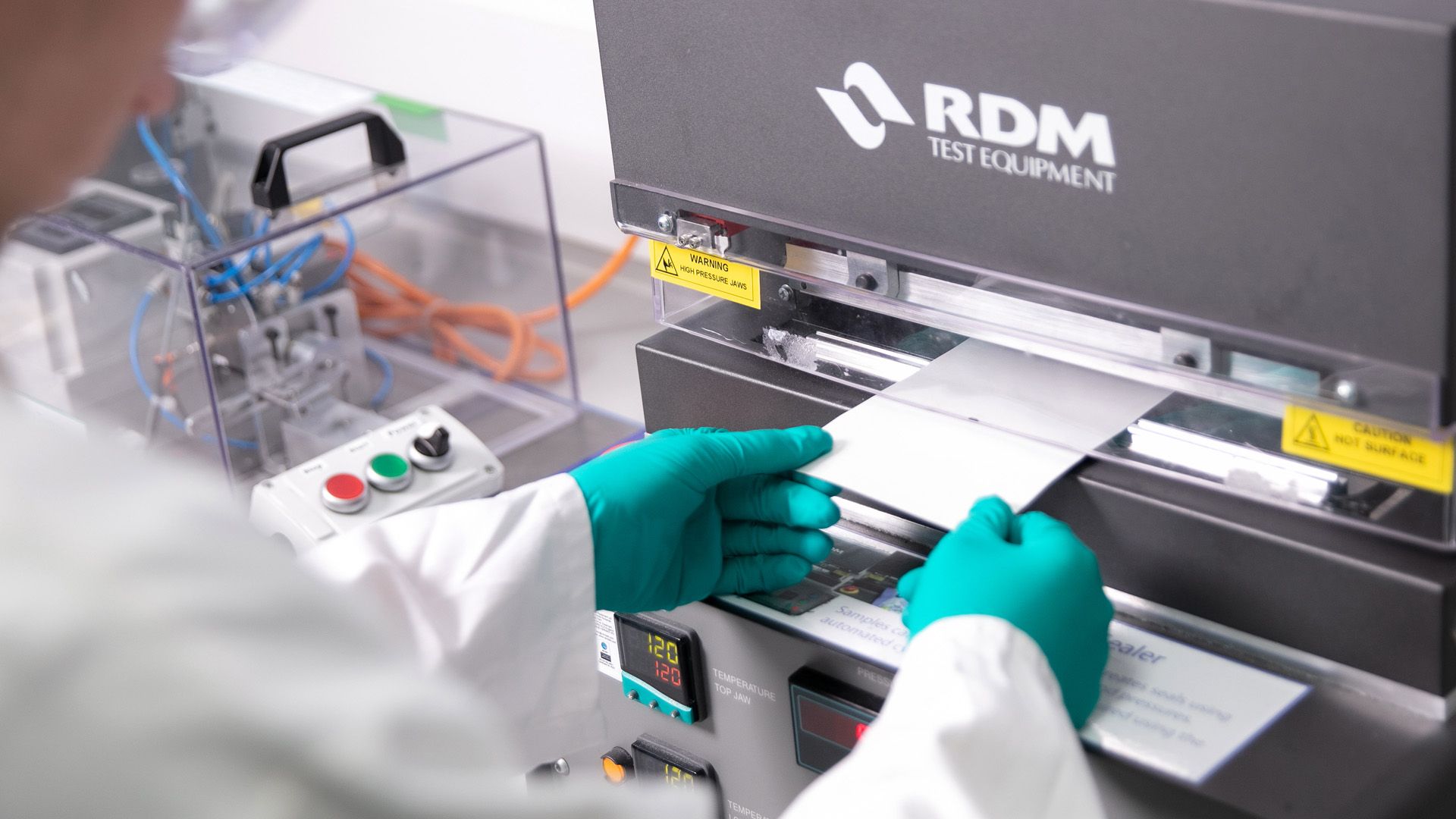 Unilever R&D scientist wearing a white lab coat and green gloves, feeding a paper packaging sample into a machine