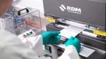 Unilever R&D scientist wearing a white lab coat and green gloves, feeding a paper packaging sample into a machine