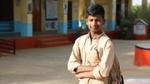 14-year-old Virendra standing with his arms folded, carrying a bag on his shoulder outside his school.