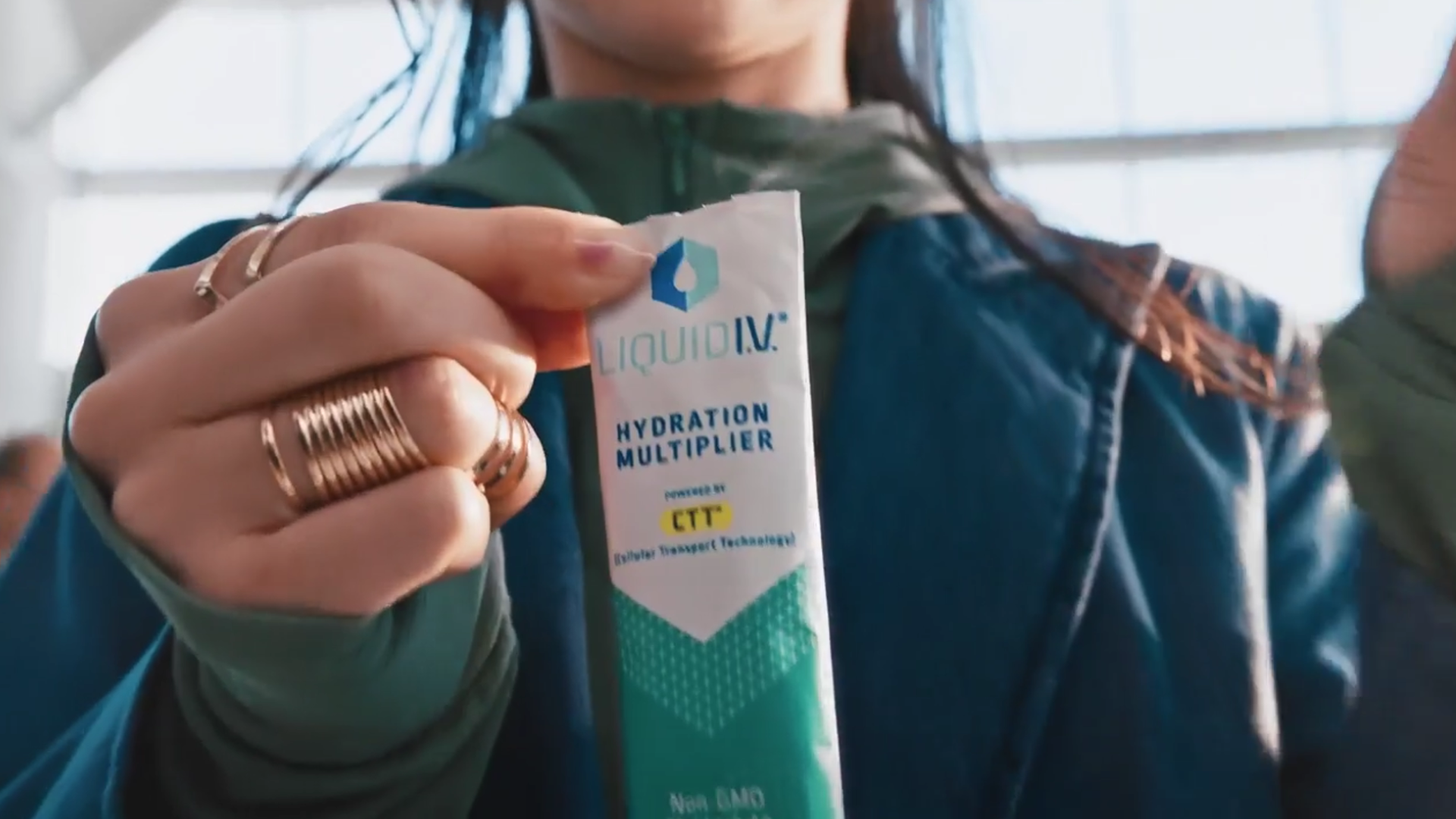 A lady in a blue coat ripping open a Liquid I.V. sachet.