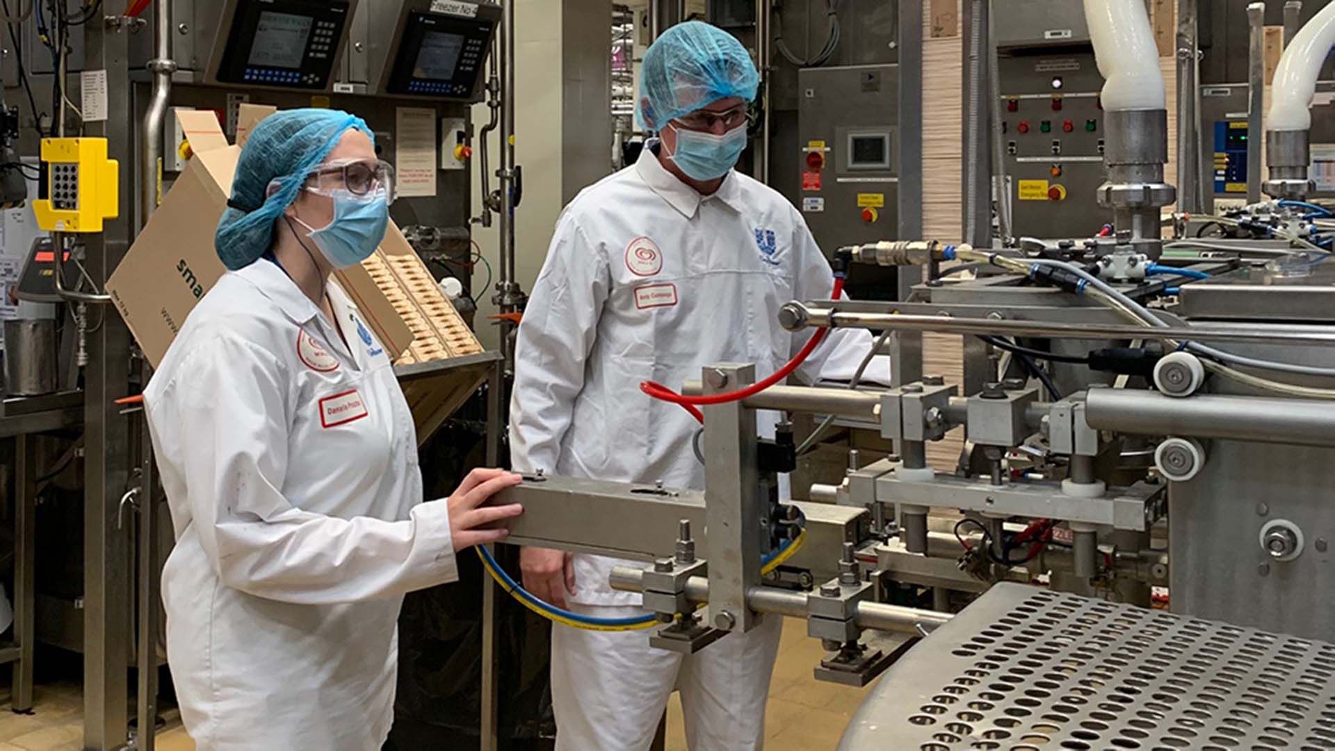 Man and women in hairnets and white coats on a factory floor checking machinery