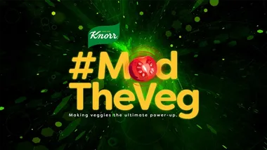 A green background with yellow text which reads: ‘#ModTheVeg’. The ‘o’ is represented by a sliced red tomato.
