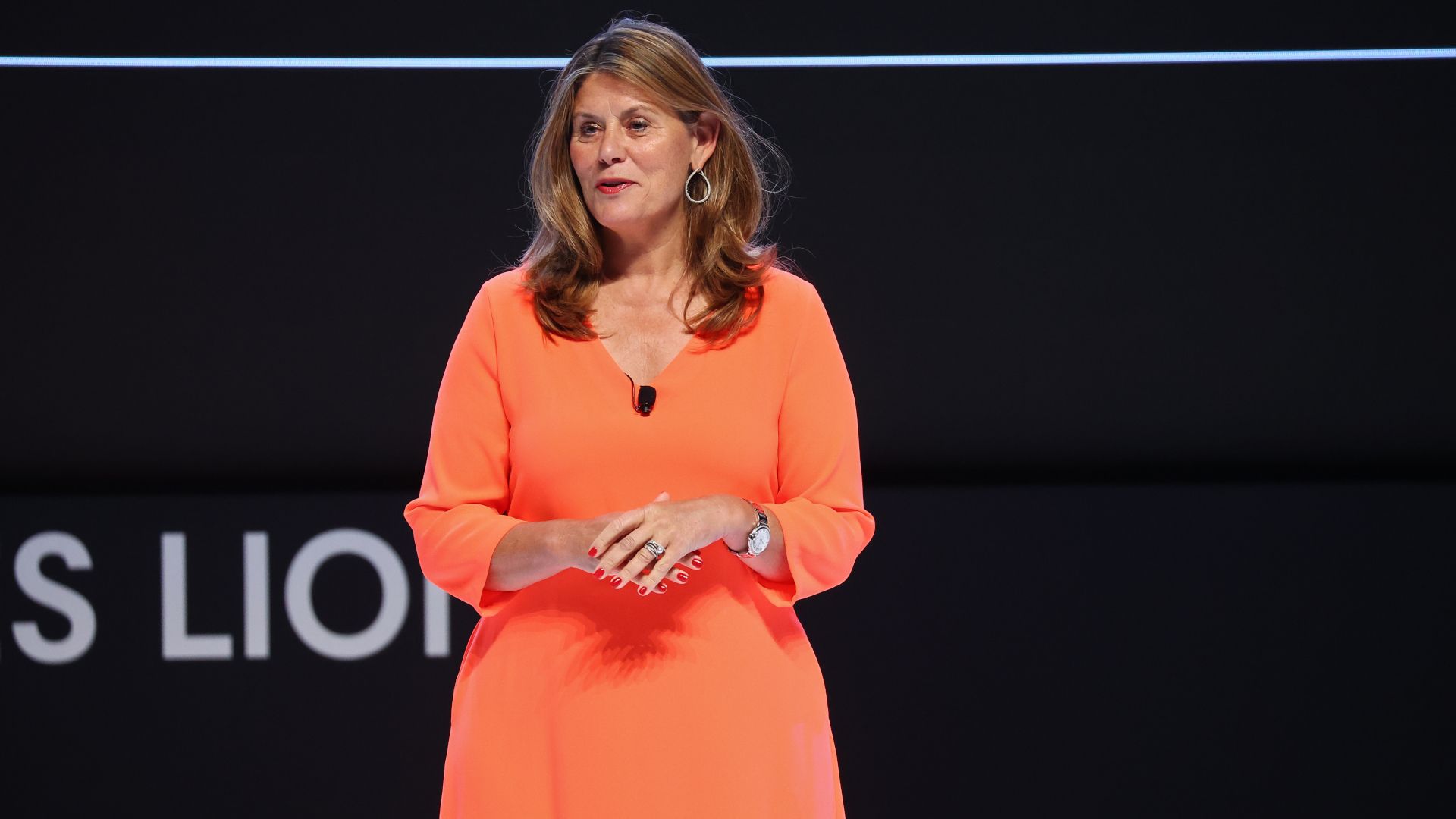Conny Braams in an orange dress speaking on stage