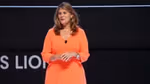 Conny Braams in an orange dress speaking on stage