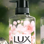 A close‑up of a LUX Botanicals liquid soap bottle with a black pump lid, decorated with pink cherry blossom illustrations.