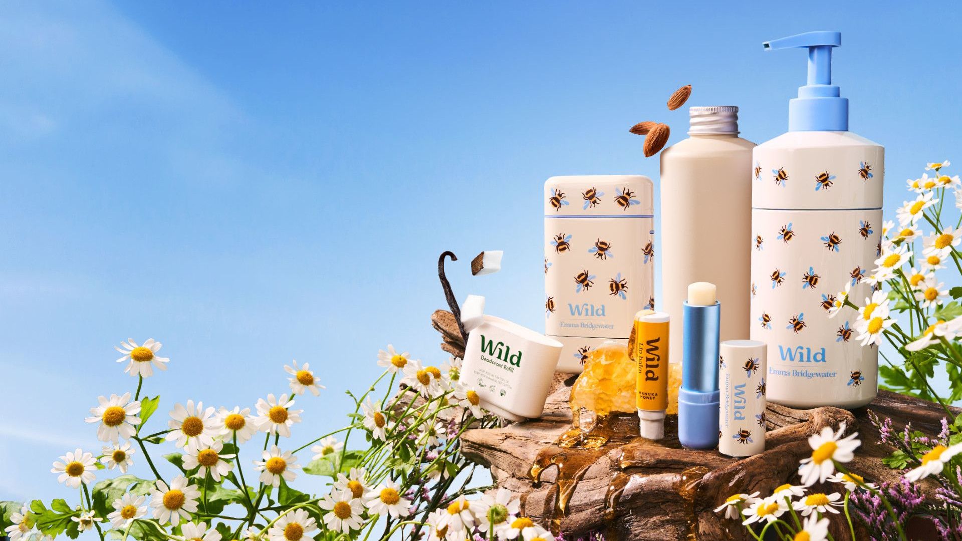 A display of Wild personal care products on a rock, surrounded by daisies with a blue sky.