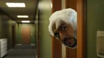 A person with a shaved beard and foam covering their head peeks through a slightly open doorway into a corridor with green walls and overhead lights.